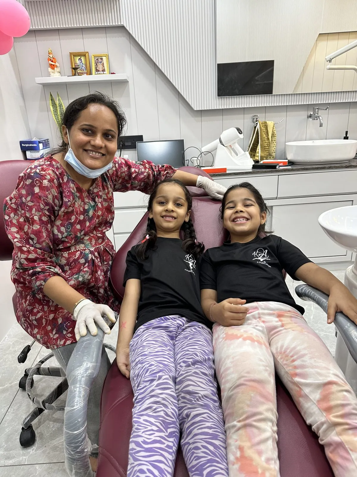 ટ્રીટમેન્ટ ચેરમાં બેઠેલી બે હસતી નાની દર્દીઓ સાથે ડૉ. રીમા શાહ